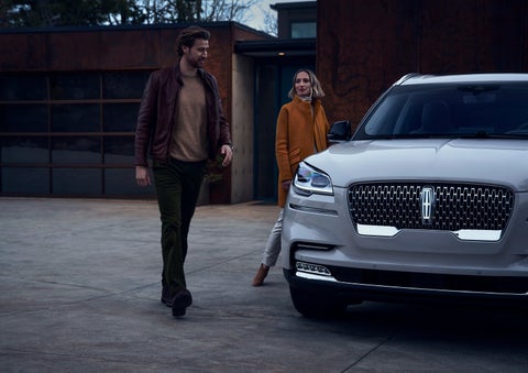 A man and a woman approaching a 2024 Lincoln Aviator® SUV, which illuminates certain lights when they are close | Buss Lincoln in McHenry IL